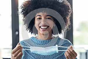 Smiling african woman taking off an hygienic mask while smiling while looking at camera at the office