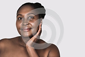 Smiling African woman touching her skin against a gray background