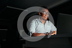 Smiling african young businessman working overtime in the office to finish the project within the deadline