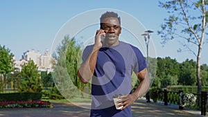 Smiling Afro-American man talking on cell phone holding white cup with coffee