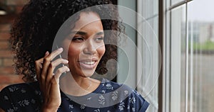 Smiling Afro American woman stand by window speak on phone