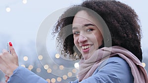 Smiling afro american woman stands outdoors in winter looking at camera smiling takes pictures on phone makes photo