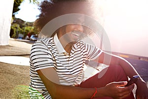 Smiling afro man sitting outside with cell phone