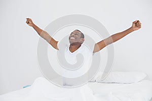 Smiling Afro man stretching his arms out in bed