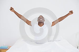 Smiling Afro man stretching his arms out in bed