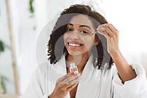 Smiling Afro Woman Applying Hydrating Face Serum On Her Beautiful Skin