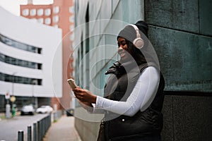 Smiling afro woman using mobile phone while standing outdoors at city street