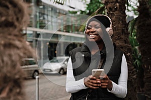 Smiling afro woman using mobile phone while standing outdoors at city street