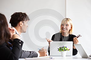 Smiling aged business woman talking and looking at colleague while team meeting, Happy attentive female team leader