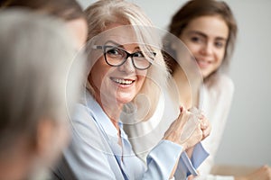 Smiling aged businesswoman looking listening to colleague at tea