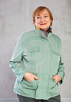 Smiling aged woman in green jacket with hands in pockets