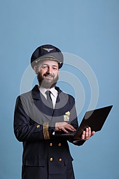 Smiling airliner pilot using laptop, typing message side view