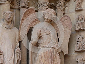 Smiling angel with beguiling smile giving a fist pump on the entrance to Notre-Dame de Reims Cathedral in France