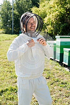 smiling apiarist adjusting beekeeping suit near