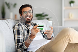 Smiling arab guy in casual holding smartphone and credit card