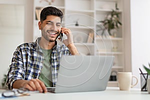 Smiling Arab man working and talking on phone at home