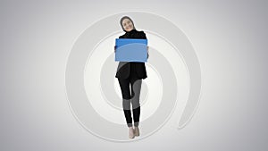 Smiling Arab woman in hijab holding blank blue poster and lookin