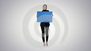 Smiling Arab woman in hijab holding blank blue poster and lookin