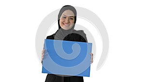 Smiling Arab woman in hijab holding blank blue poster and looking at camera on white background.