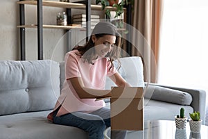 Smiling Arabian woman unpacking box, sitting on couch at home