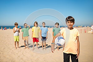 Smiling Arabic boy standing with ball on beach