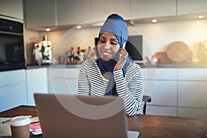 Smiling Arabic entrepreneur talking on a cellphone in her kitche