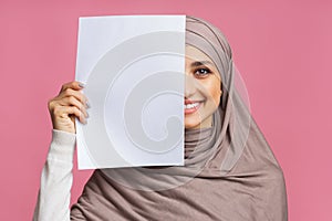 Smiling arabic girl covering half of face with blank paper sheet