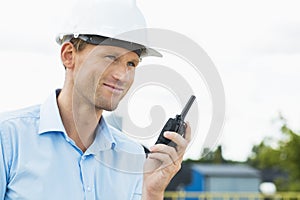 Smiling architect holding walkie-talkie at construction site