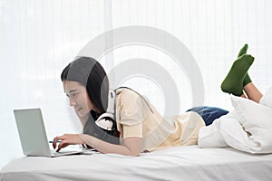 Smiling asia woman using a laptop while lying on her bed, inspiration, creativity, comfort and people concept
