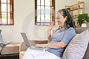 Smiling Asian-aged retired woman talking with her daughter through a video call via laptop