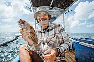 smiling Asian angler holding a grouper on small fishing boat