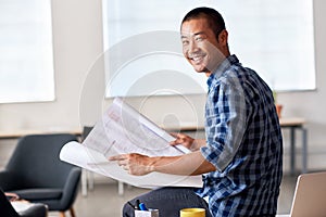 Smiling Asian architect reading blueprints in an office