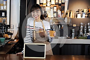 Smiling asian barista holding cup of coffee at counter in coffee