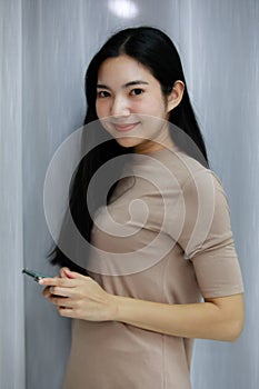 Smiling asian beautiful woman Standing wearing a Gray dress holding smartphone  in the bedroom behind a curtain. Female asia smlie