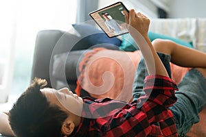 Smiling asian boy using tablet for video call, with caucasian male teacher on screen