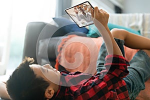 Smiling asian boy using tablet for video call, with smiling male teacher on screen