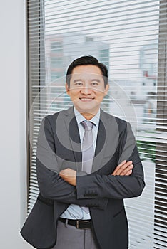 Smiling asian businesman standing by the window.