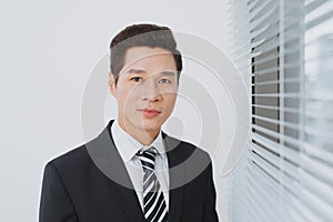 Smiling asian businesman standing by the window.