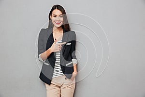 Smiling asian business woman with arm in pocket pointing away
