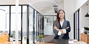 Smiling asian business woman pointing up and looking at the camera at her office. copyspace.