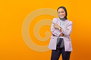 Smiling Asian business woman pointing up and looking at camera over yellow background