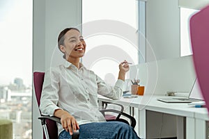Smiling asian business woman sitting in office on her workplace and looks away