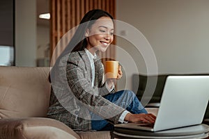 Smiling asian business woman working laptop and drink coffee sitting in cozy cafe