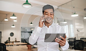 Smiling Asian businessman using a cellphone and tablet at work