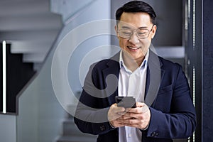 Smiling Asian businessman using smartphone in modern office
