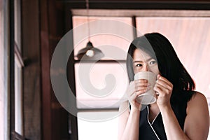 Smiling Asian businesswoman is relaxing and drinking a cup of hot coffee in coffee shop