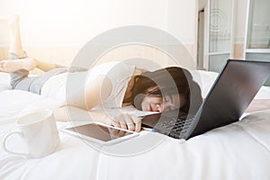 Smiling Asian businesswoman is relaxing and laying with laptop in bedroom on holiday. She so tried for online working from home