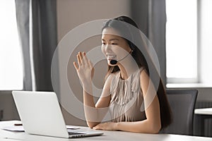 Smiling asian businesswoman wearing wireless headset waving doing video chat