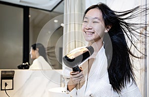 Smiling asian child girl drying hair with hairdryer,beautiful woman in bathrobe blow drying with hair dryer after hair washing,