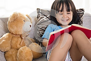 Smiling Asian Chinese little girl reading book with teddy bear